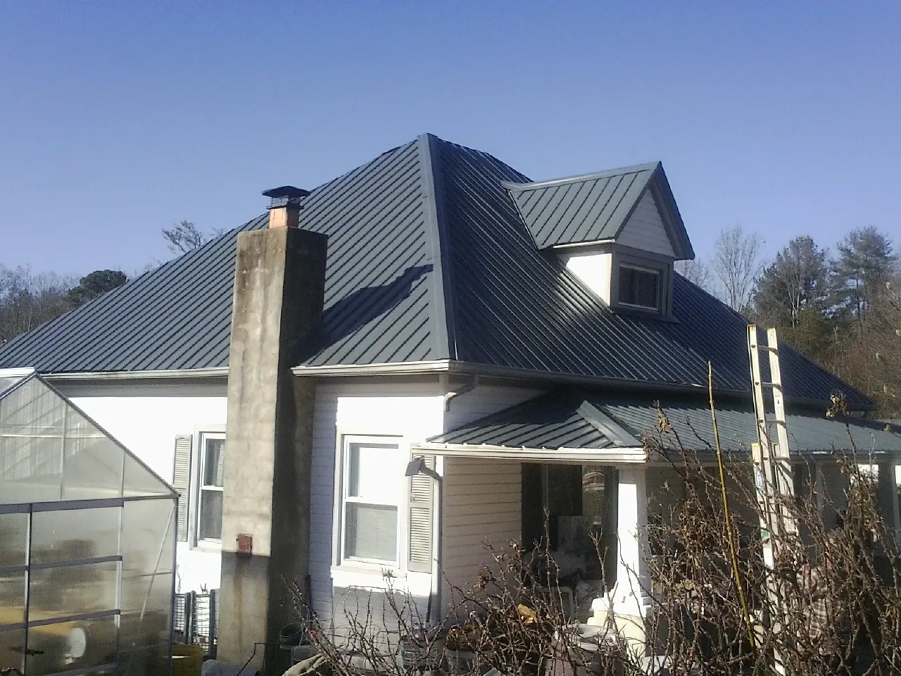 Dark blue standing seam metal roof on a white farmhouse with dormer — Slate & Tile Roof Repair by Roofing Brothers in Stedman