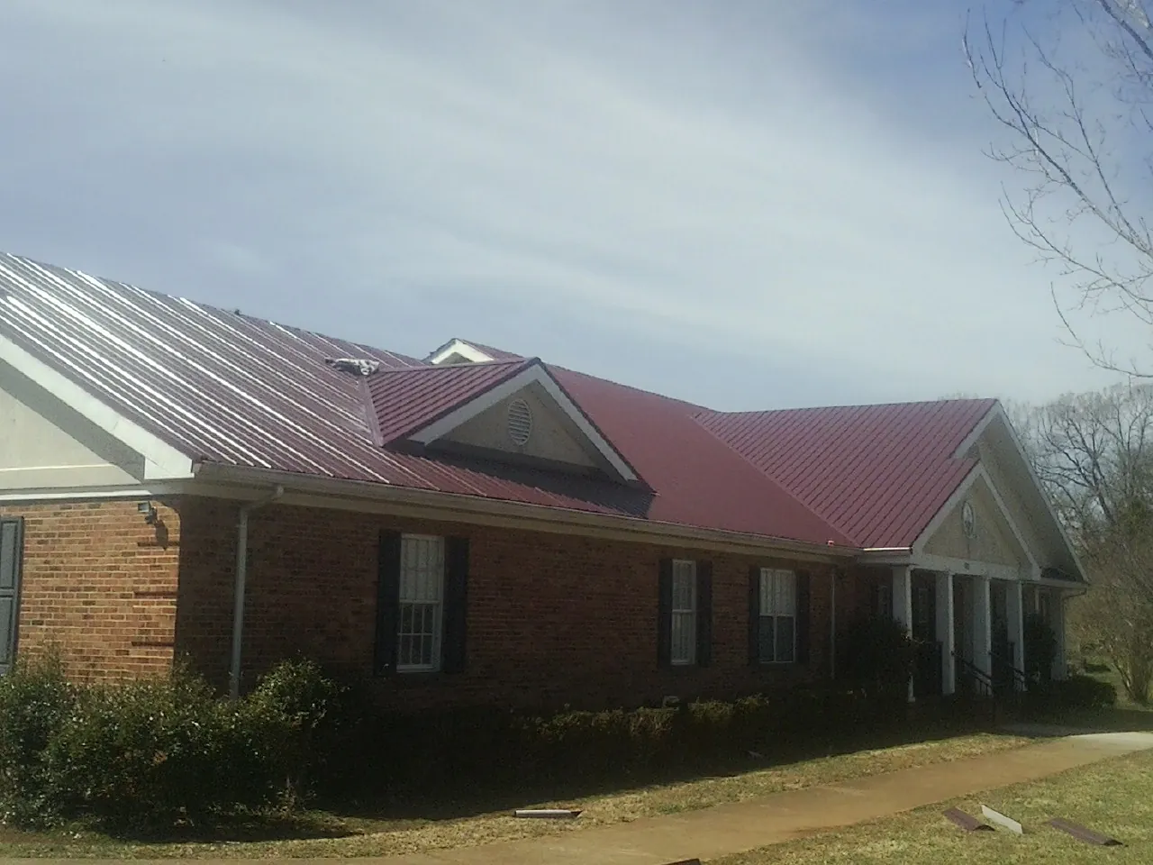 Red metal roof with gabled entries on a long brick building, from a Hail Damage Roof Repair job in Stedman
