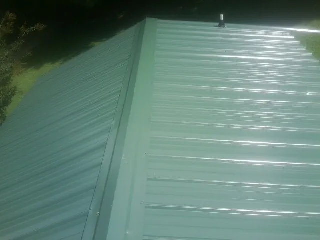 New green metal panels meeting at the ridge of a roof — Flat Roof Repair work by our crew in Stedman