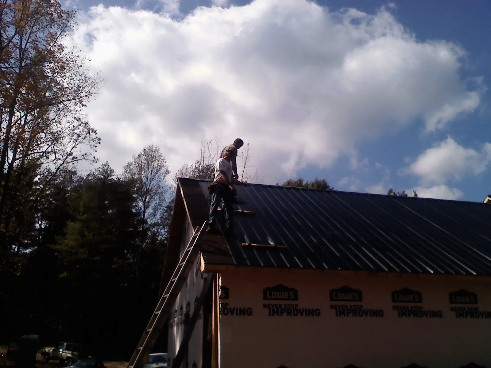Roofer fastening dark metal panels high against a cloudy sky, from a Roof Inspection job in Stedman
