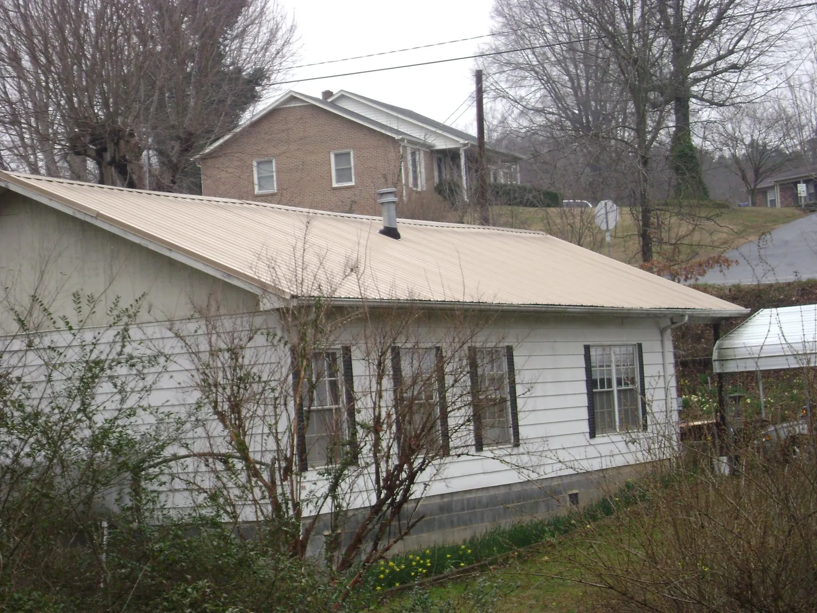 Tan metal roof on a white sided house set into a hillside — Commercial Roofing by Roofing Brothers in Stedman