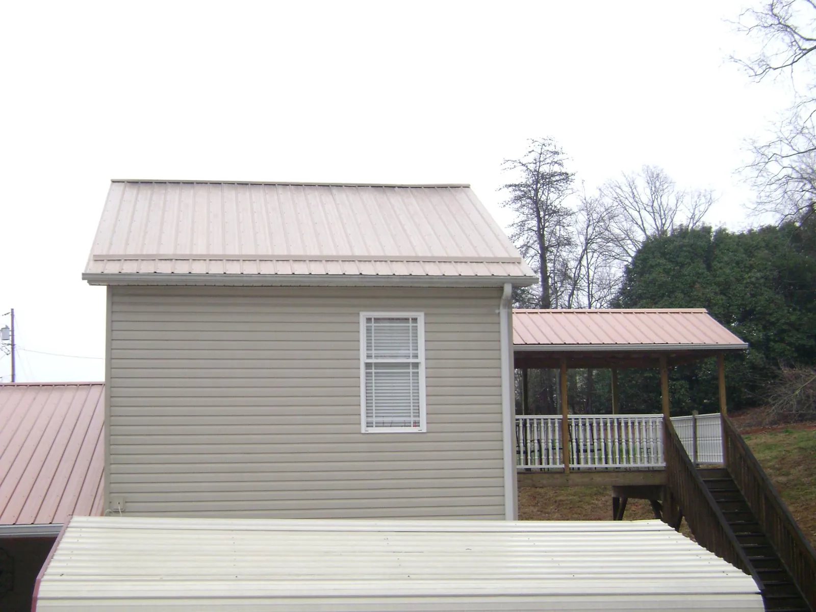 Tan metal roofs on a two story addition and attached porch, from a Roof Replacement job in Stedman